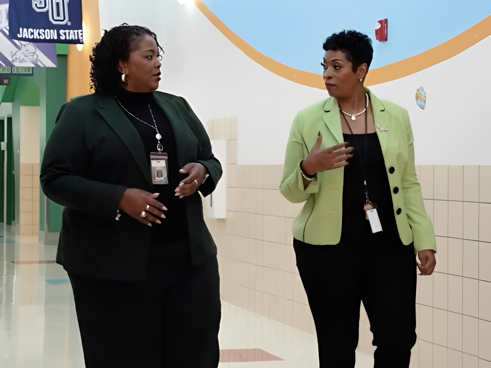 Two women walking and talking in hallway.