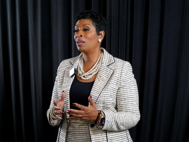 Woman speaking in front of black curtain.